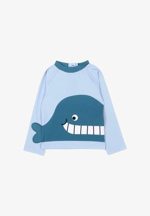 Jasnoniebieska koszula z długim rękawem z grafiką uśmiechniętego ciemnoniebieskiego wieloryba, z naszytym ogonem po jednej stronie i wysokim kołnierzem.