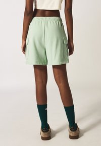 Pantaloni cargo verde menta con vita elastica, tasche laterali, materiale in cotone, abbinati a calze rigate verde scuro e calzature beige.