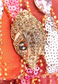 Gouden handvormige hardware met ingebedde bruine kristallen, omringd door oranje netting en roze pailletten. Geweven en intricaat gedetailleerd ontwerp.
