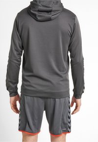 Hoodie de sport gris avec une texture, associé à un short gris assorti avec des accents orange et des motifs noirs sur les côtés.