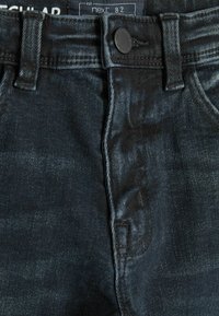 Jeans de mezclilla oscura con una textura suave, que presentan un cierre de botón, un diseño de cinco bolsillos y un sutil desgaste a lo largo de la tela.