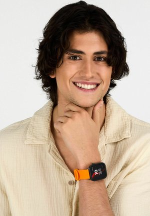 Orologio intelligente con quadrante quadrato nero e vivace cinturino in silicone arancione, indossato su un polso. La maglietta è di un beige chiaro con una trama in tessuto.
