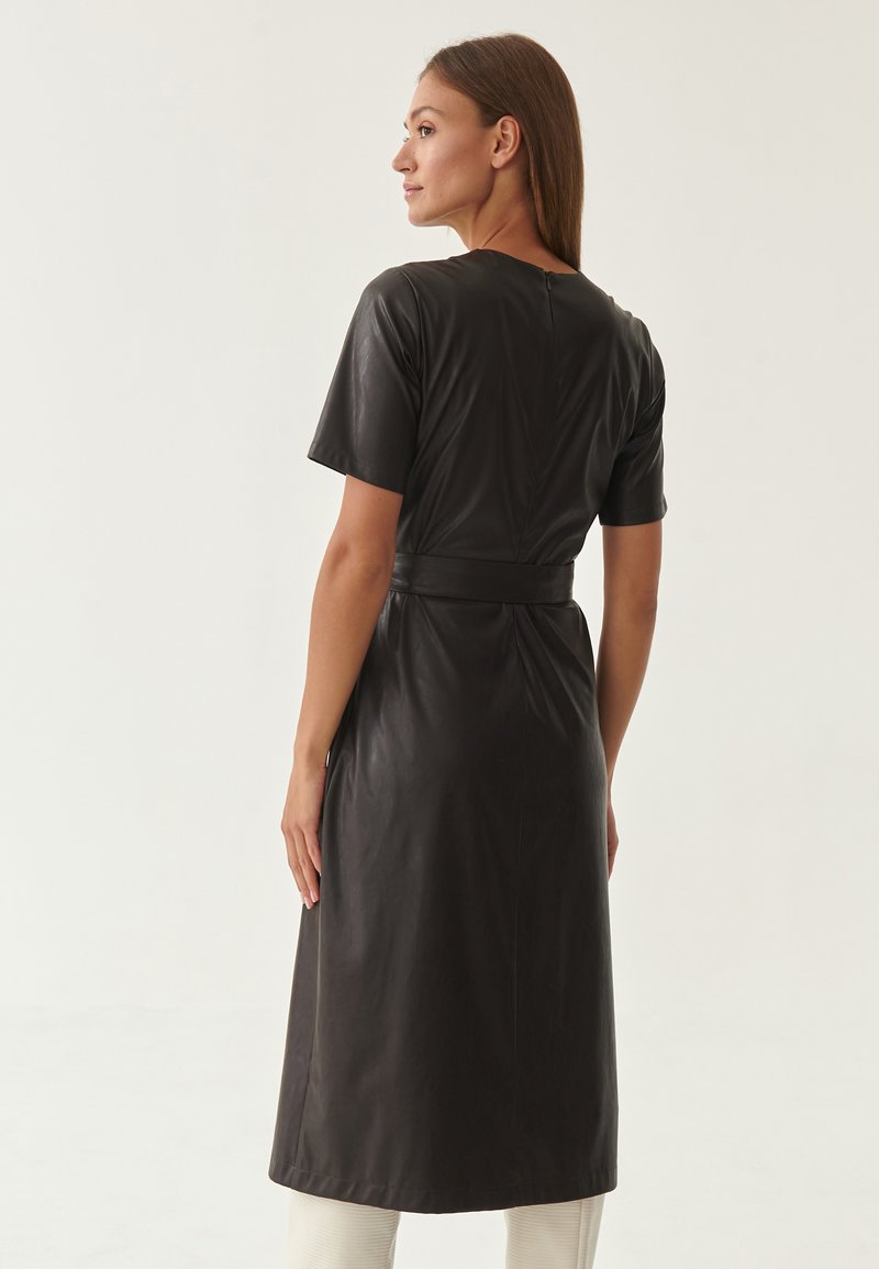 Abito in pelle nera con maniche corte, una cintura in vita e lunghezza fino al ginocchio. Texture liscia con silhouette aderente e dettaglio della cucitura posteriore.