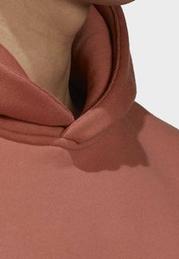 Närbild av nacke och axel som bär en dämpad rosafärgad huoodie med vikbar krage mot en enkel bakgrund.