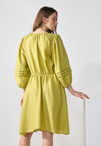 Langärmliges, gepufftes Kleid aus strukturiertem, hellgrünem Stoff. Verfügt über eine lockere Passform mit einem elastischen Bund und subtilen Faltenakzenten.
