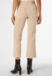 Jeans beige de campana con una cintura de altura media, bolsillos traseros y dobladillo deshilachado, combinados con botas negras brillantes hasta el tobillo. Material de algodón.