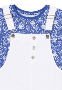 Pantalones de tirantes de mezclilla blanca con herrajes plateados, que presentan una tela con un estampado floral azul en la parte superior. Tres botones destacan en la parte delantera.