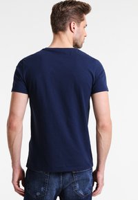 Navy blue cotton t-shirt with a round neck, short sleeves, and a plain back design. Worn with faded blue jeans.
