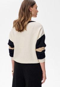 Crèmekleurige en marineblauwe pullover met gestructureerde mouwen met beige strepen. Zacht materiaal, cropped ontwerp en geribbelde manchetten.