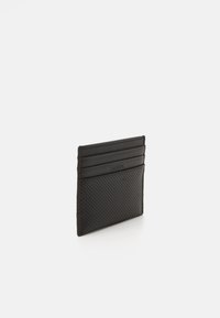 Cardholder negru realizat din piele texturată, cu patru sloturi verticale pentru carduri și un design perforat pe spate. Logo-ul Lacoste embosat.