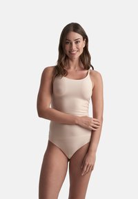 Canotta beige con spalline sottili, caratterizzata da un design aderente e una texture liscia. Abbinata a un paio di slip in stile bikini dello stesso colore.