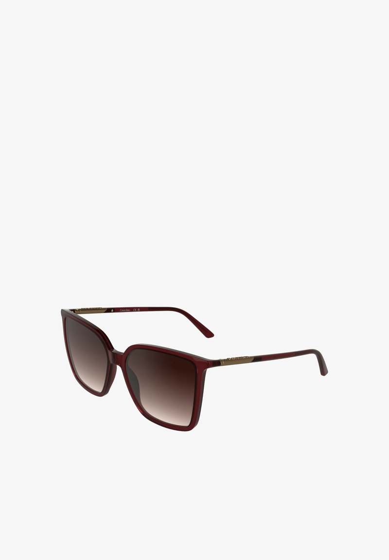 Lunettes de soleil avec une monture carrée en plastique bordeaux. Verres dégradés marron foncé, accents métalliques dorés sur les branches. Finition polie.