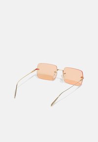 Ochelari de soare pătrați cu lentile de un portocaliu deschis și rame din metal aurit. Caracteristici: brațe subțiri și pedale nazale transparente. Design minimalist.