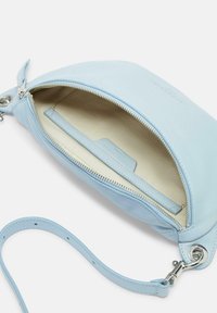 Borsa in pelle azzurro chiaro con chiusura a zip e foderatura beige. Presenta uno slot per carte e una tracolla removibile. Texture liscia e design semplice.