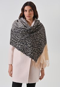 Sciarpa a pois di leopardo realizzata in tessuto morbido, con sfumature di grigio e beige, bordata di frange, appoggiata su un cappotto rosa chiaro.