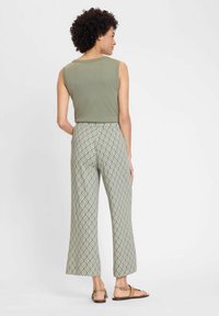Olive green sleeveless top with a scoop neckline, paired with patterned wide-leg pants in green and white diamond shapes. Brown sandals.
