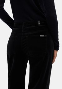 Czarne spodnie sztruksowe o wąskim kroju, wyposażone w dwie tylne kieszenie oraz subtelny znaczek marki w pobliżu prawej kieszeni. Gładka faktura.