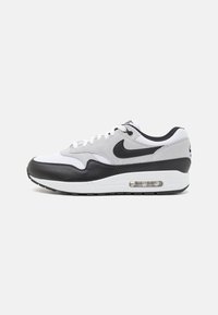 Nike Air Max 1-sneaker i svart, vitt och grått. Har en överdel av läder och tyg, nätpaneler och en synlig luftkudde i sulan.