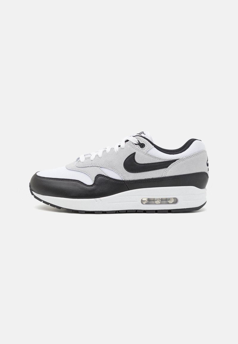 Nike Air Max 1-sneaker i svart, vitt och grått. Har en överdel av läder och tyg, nätpaneler och en synlig luftkudde i sulan.