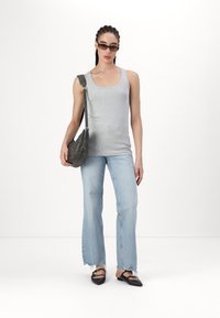 Graues enges Tanktop, hellblaue Schlagjeans mit ausgefransten Säumen, schwarze Ballerinas und eine graue Umhängetasche. Trägt dunkle Sonnenbrillen.