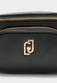 Mustast nahkakott kuldse t�õmbluku ja logoga. Sile tekstuur, ümar kuju ja minimalistlik disain.