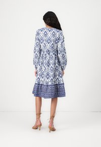 Rochie cu mânecă lungă, albă, cu un model floral albastru ornamentat, tiv evazat și talie elastică. Asortată cu sandale cu toc cu bretele bej.