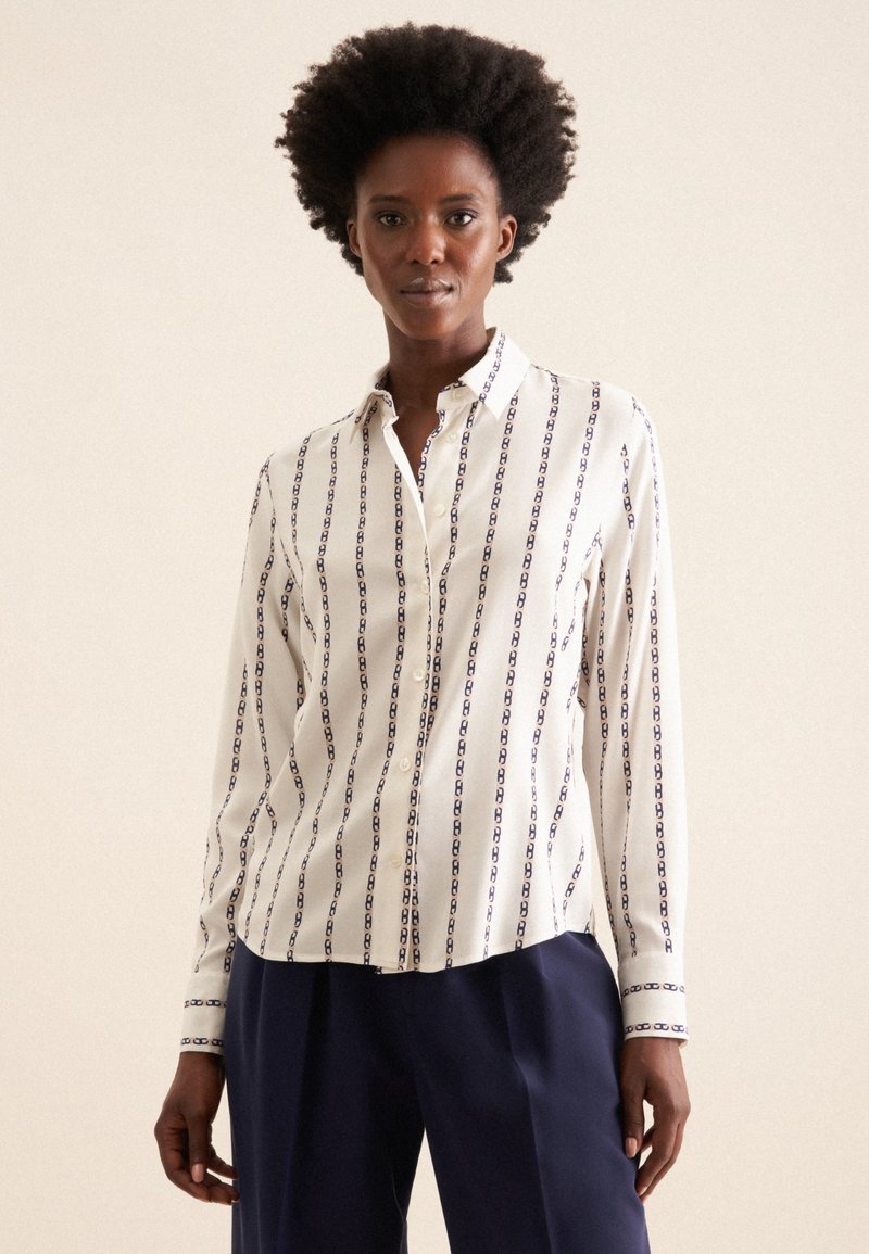 Weißes Hemd mit vertikalem blauen Kettenmuster, Button-Down-Kragen und langen Ärmeln. Verfügt über einen geraden Schnitt und Manschetten mit blauen Akzenten.