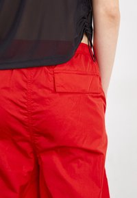 Shorts légers rouges dotés d'une poche arrière et d'une taille élastique, accompagnés d'un haut noir transparent avec un cordon de serrage. Texture lisse.
