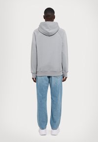 Felpa con cappuccio grigia chiara dal taglio morbido e polsini a costine, abbinata a jeans a gamba dritta blu chiaro e scarpe bianche.