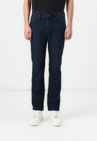 Jeans din denim albastru închis cu croială dreaptă, având buzunare frontale, bucle pentru curea și un finisaj texturat discret. Puși în completare cu adidași albi.