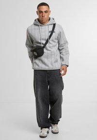 Felpa grigia a strisce con tasca frontale, abbinata a jeans neri larghi. Un piccolo borsello a tracolla nero con logo completa il look.