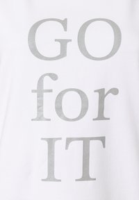 Witte t-shirt met metallic zilveren tekst "GO for IT." Het materiaal is glad katoen, met een casual pasvorm en zonder extra patronen.