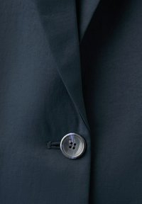 Close-up of a dark navy blazer with a single shiny four-hole button fastened at the front.