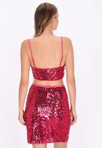 Rózsaszín flitteres anyagból készült, testhez simuló kétdarabos szett, vékony pántos crop top és hozzá illő, térd középig érő szegéllyel rendelkező ceruzaszoknya.