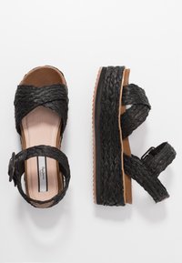 Svarta vävda plattformssandaler med korsremdesign, texturerad ovandel, justerbar spännesrem och ljusbrun vadderad sula.