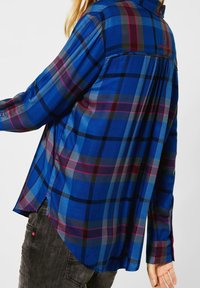 Blue plaid shirt with long sleeves, featuring varied shades of blue, gray, and pink, and a slight hi-low hem design.