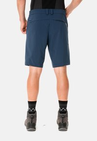Shorts de senderismo azul marino con una textura suave, que cuentan con un bolsillo trasero y pasadores para cinturón, combinados con zapatos de senderismo grises y calcetines negros con un patrón.