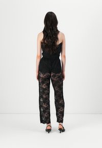 Combinaison en dentelle noire avec un corsage ajusté et des pantalons larges. Présente des motifs floraux complexes et une texture transparente dans l'ensemble.