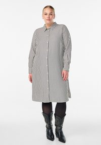 Pasiasta sukienka koszulowa w czarno-białe paski, z długimi rękawami i luźnym krojem, zestawiona z czarnymi kowbojkami z ćwiekami.