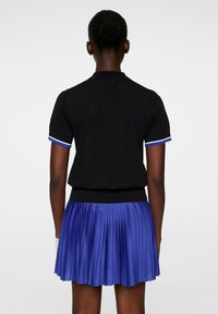 Svart kortärmad polotröja med texturmönster och vitblå ränder vid manschetterna, ihopparad med en veckad kungarblå kjol.