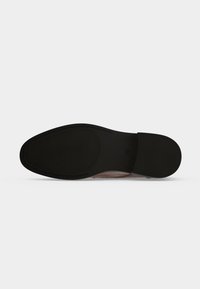 Semelle en caoutchouc noir d'une chaussure formelle marron avec une surface texturée sur l'avant-pied et le talon, sur un fond clair uni.