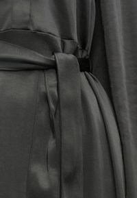 Suur lähivõte tumedast hallist terrorõngast, mis on vöödud vööga sama kangast, mis on seotud laisasse sõlme.