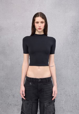 Top corto negro con mangas cortas, hecho de tela elástica. Combinado con pantalones cargo negros de tiro alto que cuentan con bolsillos y cierre de botón.