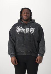 Juodas zip-up džemperis su išblukusiu efektu, turi baltą grafikos spaudą priekyje. Jame yra reguliuojamas kapišonas ir priekinės kišenės.