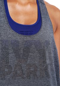 Canottiera atletica grigia con design in mesh traspirante, caratterizzata da ampie lettere perforate "IVY PARK" e un colletto interno blu a contrasto.