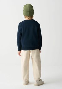 Námornícky modrá mikina, zmes bavlny, rebrované manžety, spárovaná s krémovými, voľne strihanými nohavicami a svetlými teniskami, doplnená zelenou pletenou čiapkou.