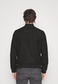 Black bomber jacket made of suede-like material, featuring a ribbed collar and cuffs, with a streamlined design and minimalistic detailing.