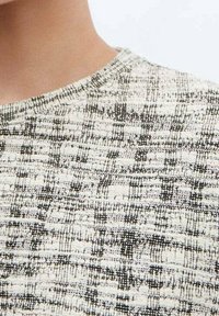 Maglione a maglia strutturata con collo rotondo, caratterizzato da una palette di colori neutra bianca e nera, e un motivo a scacchi.