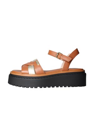 Sandalo con piattaforma con suola nera spessa, cinturini in pelle color cuoio, dettagli metallici e fibbia regolabile alla caviglia, mostrato di profilo su sfondo bianco.