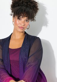 Lager utstyr med en gjennomsiktig marineblå cardigan, dyp lilla topp og en glatt tekstur. Store sirkulære øredobber og naturlige krøller fullfører stilen.